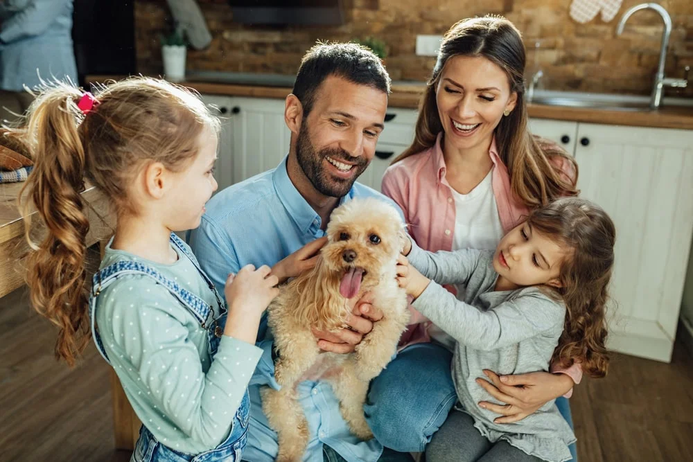 A family with two young girls pets their medium-sized dog.