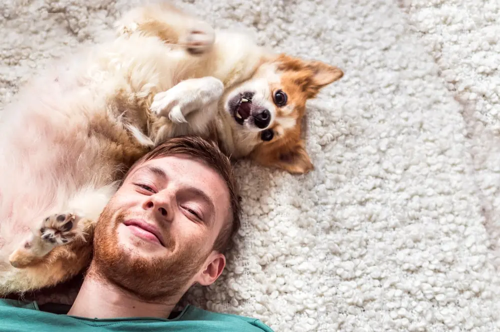 A man and his small dog lay on their backs on a carpet.