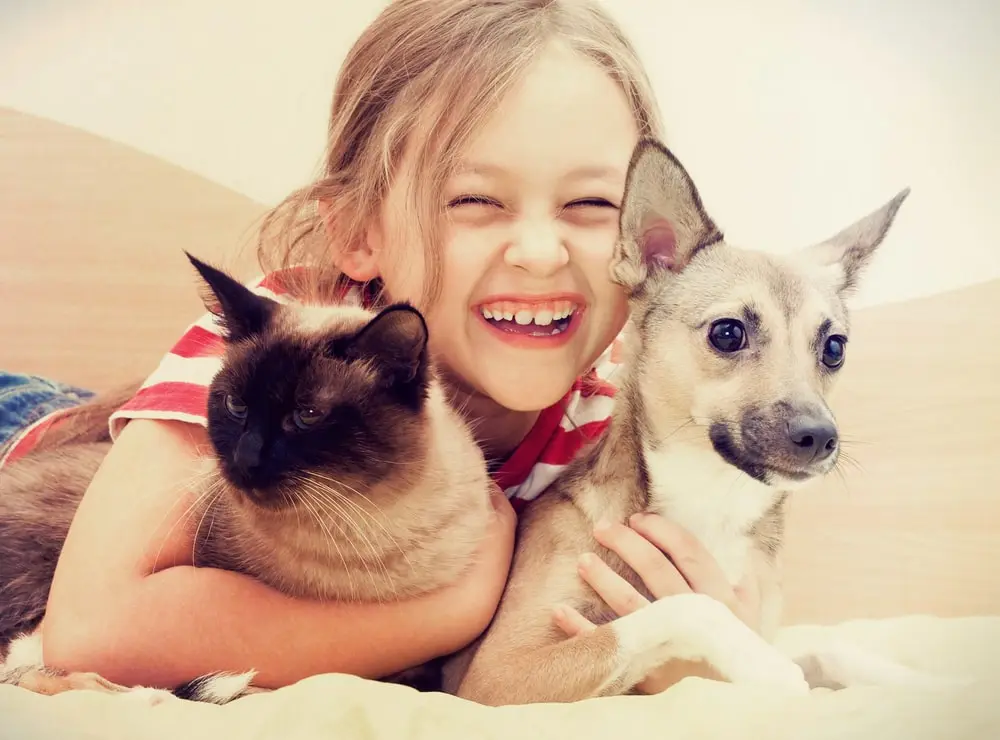 Young girl smiling while hugging a cat and dog