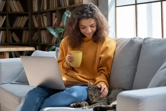 Girl sitting on a couch with a mug in her hand and petting a cat