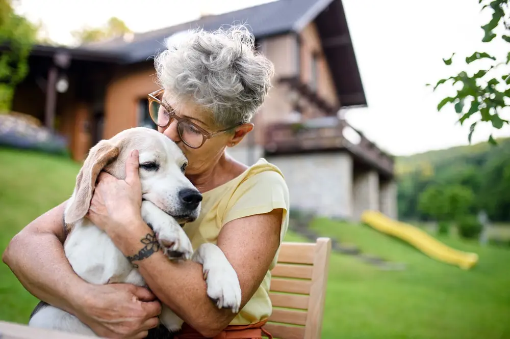 Senior woman sitting outside, kissing her dog.