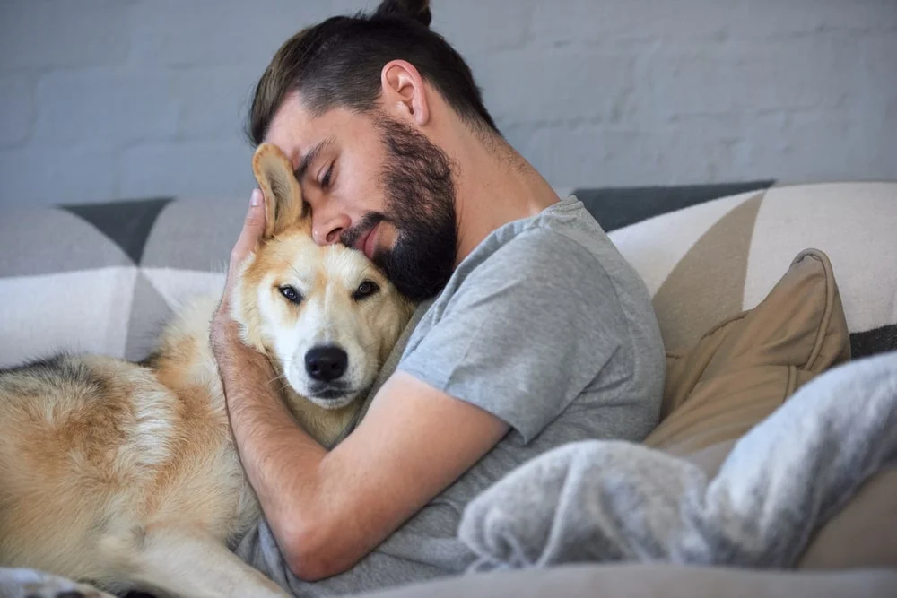 A man hugs his dog while they lay together on a couch. 