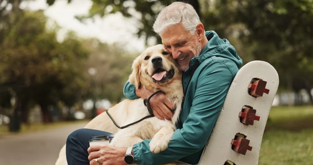 old man cuddling a dog on a park bench