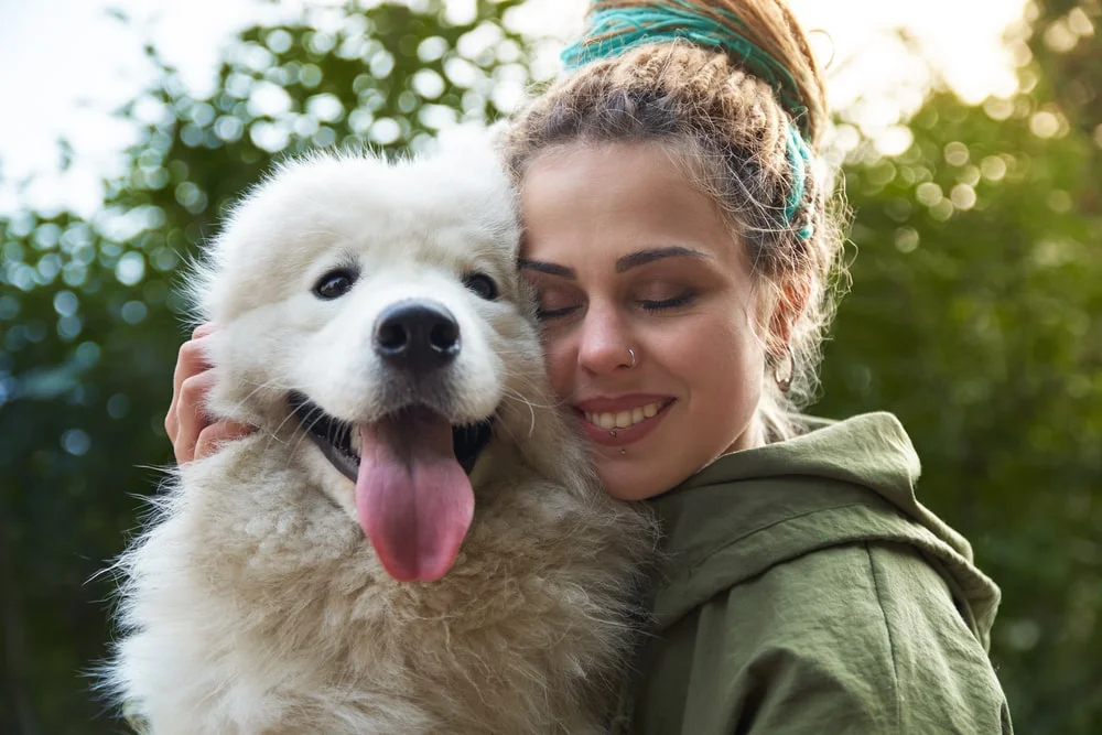 A person hugs a fluffy white dog.