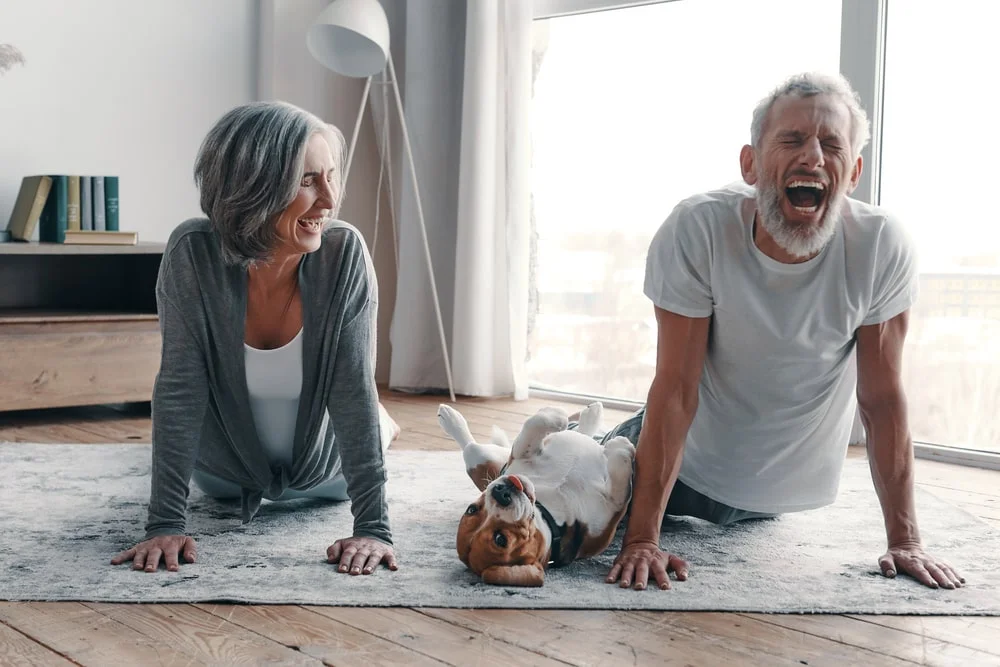 A senior couple doing yoga at home with their dog. 