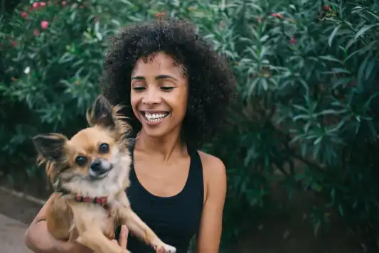 Young smiling Black woman holding a fluffy Chihuahua.