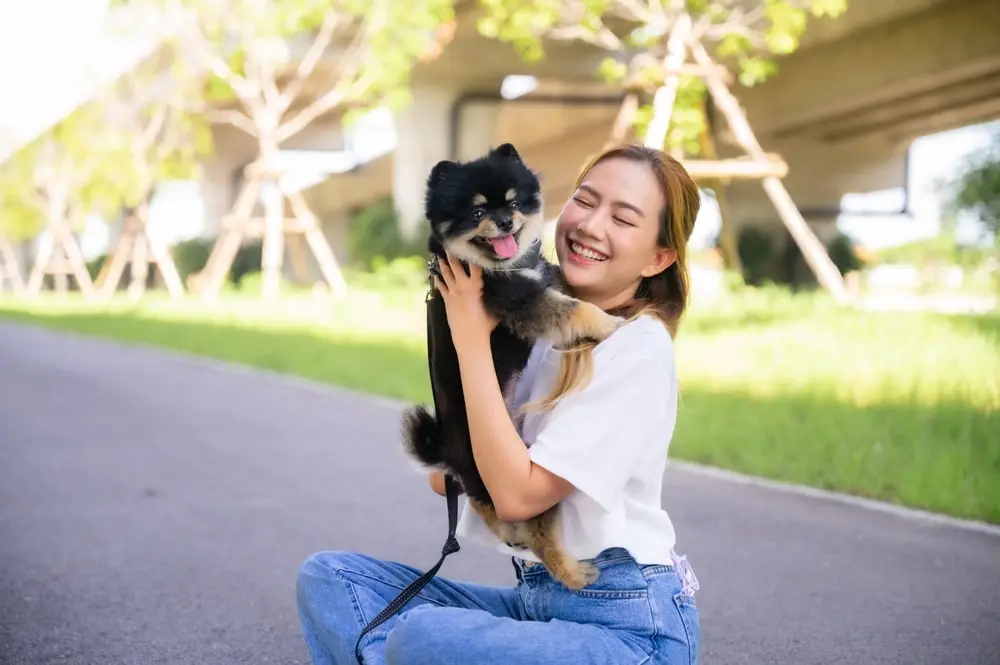 A happy young Asian woman playing with her dog outside.