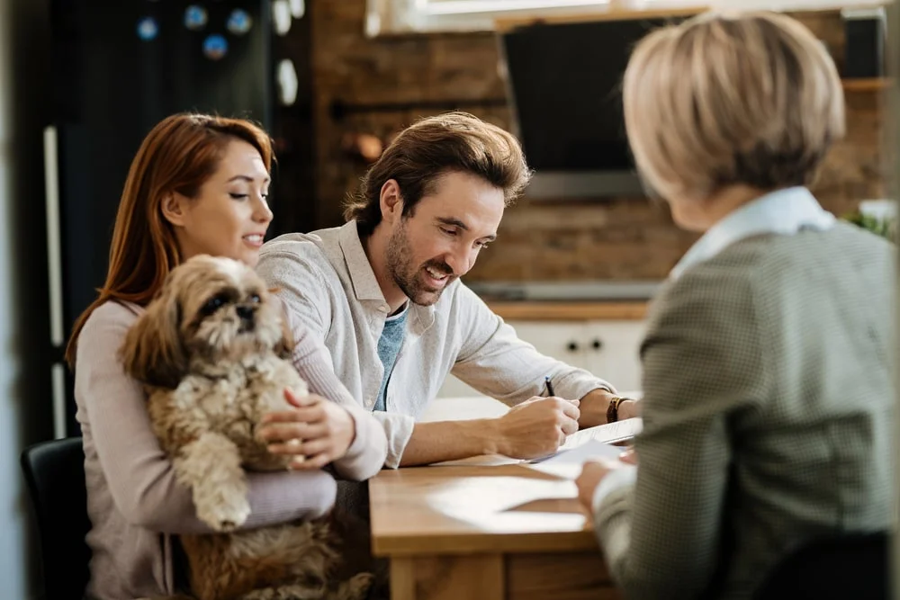 Happy man signing a contract while being with his wife on a meeting with financial advisor.