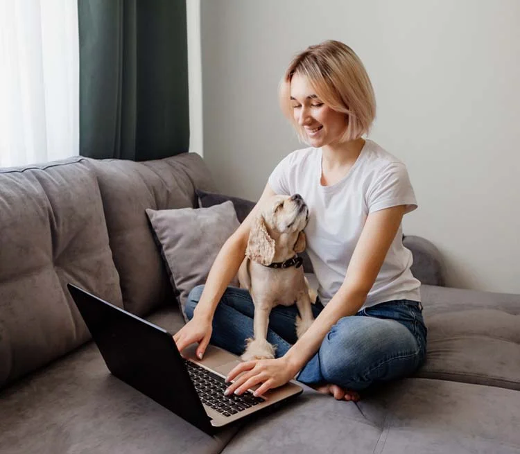 woman with a laptop sitting on her couch with her dog