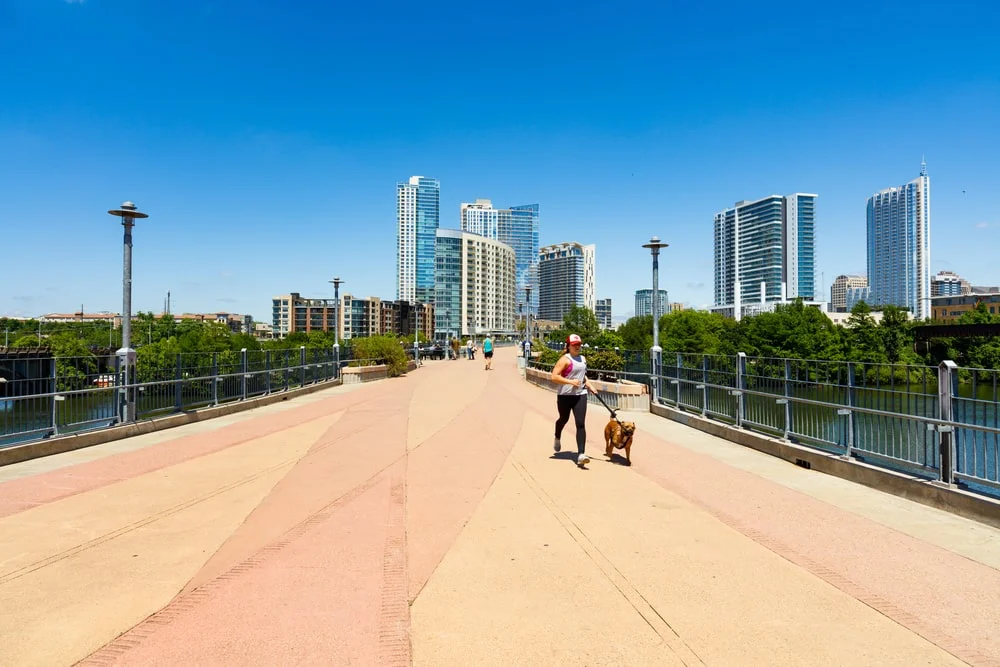 A woman and her dog walk across a bridge on a sunny day. 